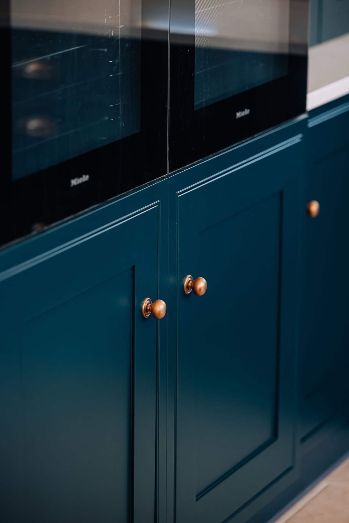 Armac Martin handmade brass knobs on blue cabinetry beneath a bank of ovens in a kitchen