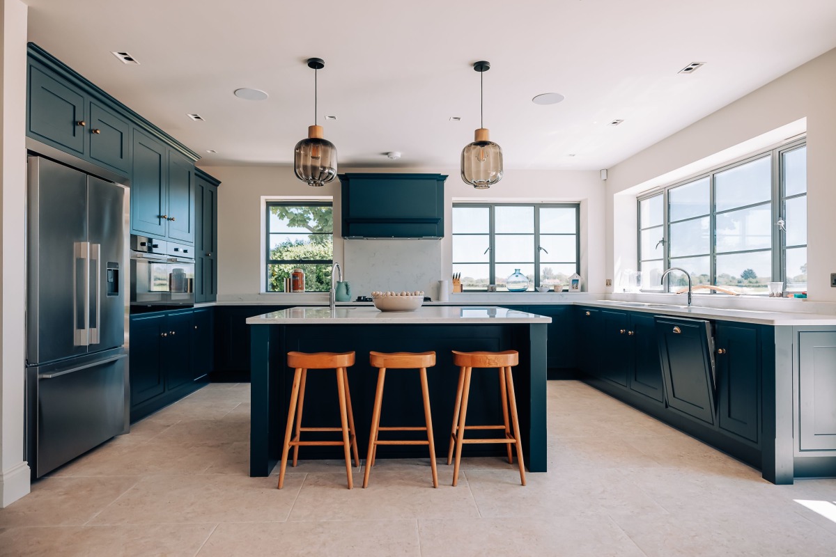 A Dark blue shaker kitchen with wooden stools and Stainless steel american fridge freezer and brass handles