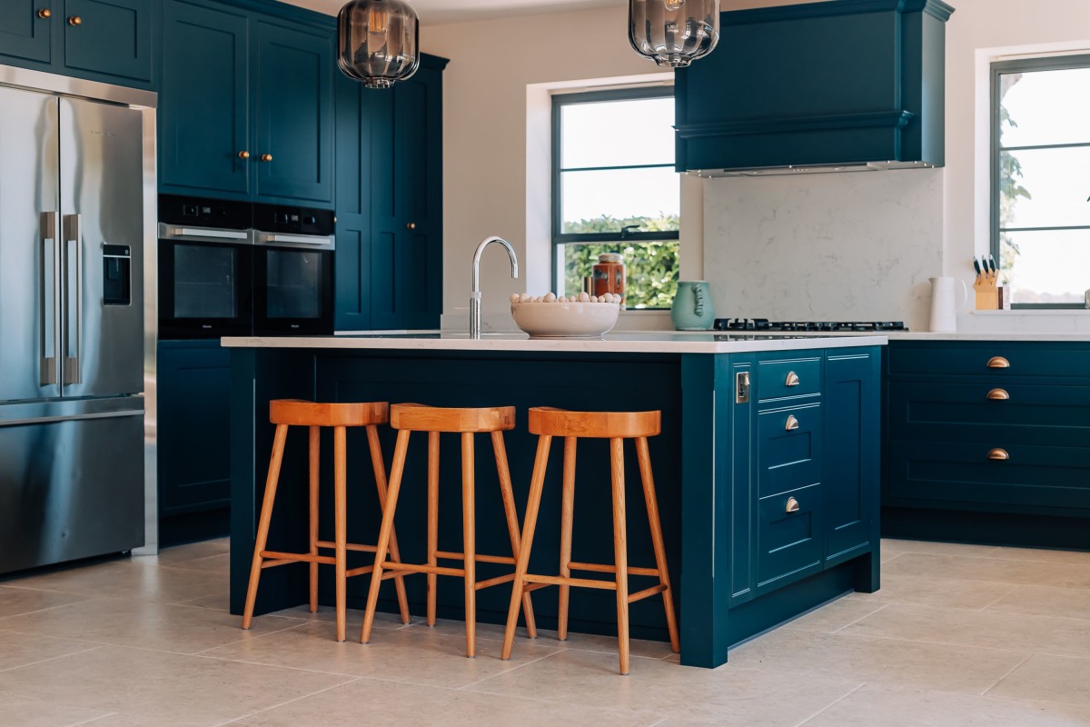 A contemporaty kitchen with dark blue in frame shaker cabinetry, wooden stools and white quartz worktops