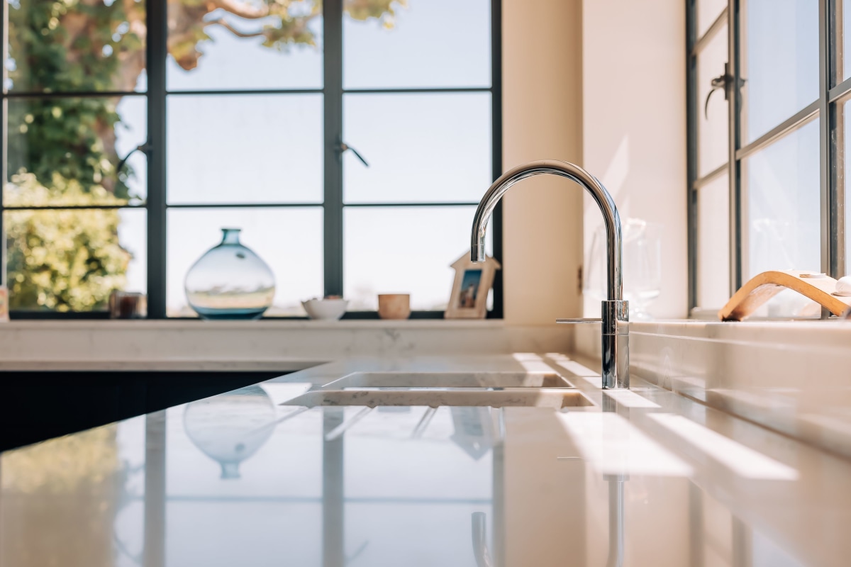 A sink set in white quartz worktops, surrounded by architectural windows