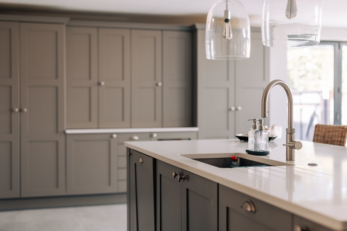 A grey - beige shaker kitchen with white quartz worktop and Quooker tap.