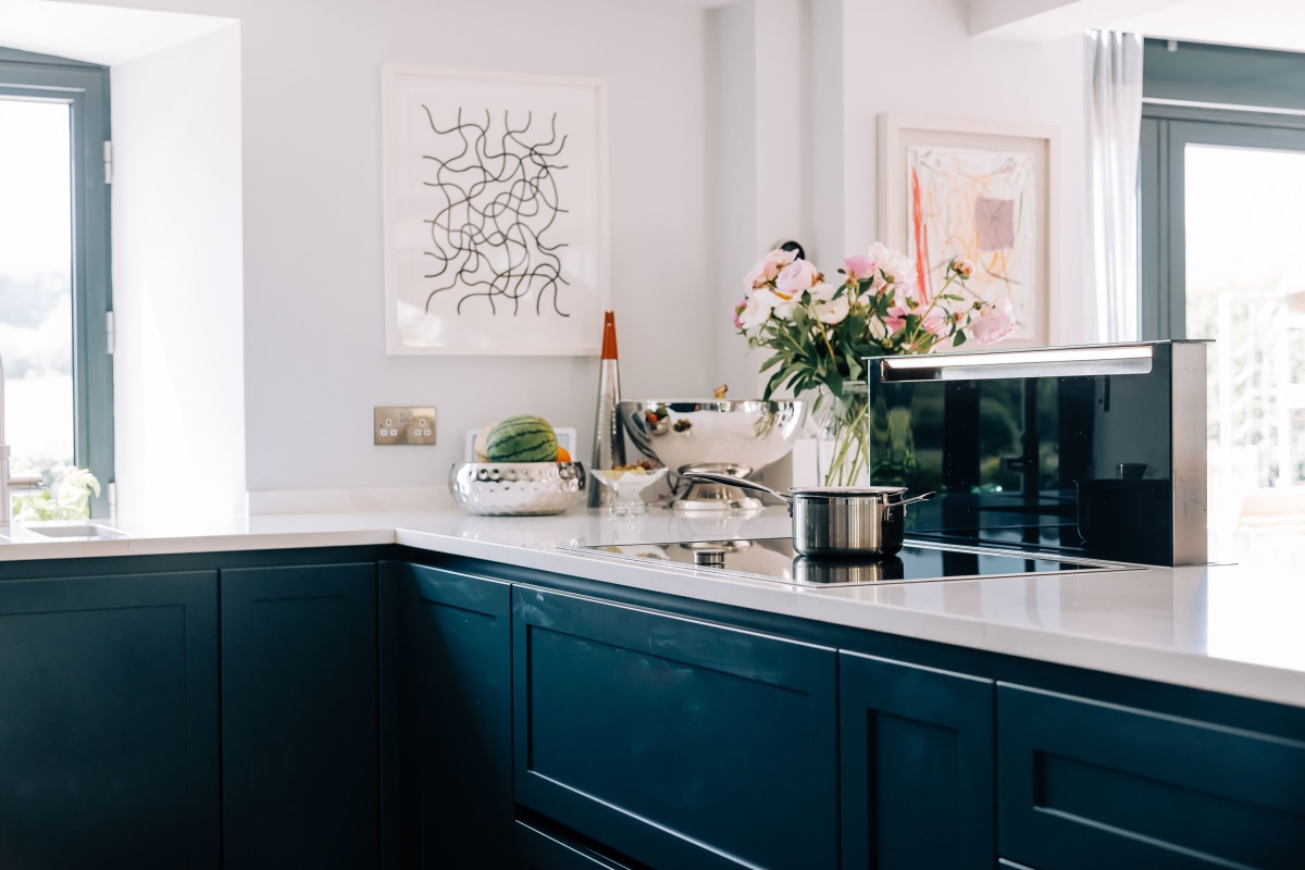 A kitchen peninsular with dark blue cabinetry, white quartz worktops and a gaggenau induction hob with retracting downdraft extractor