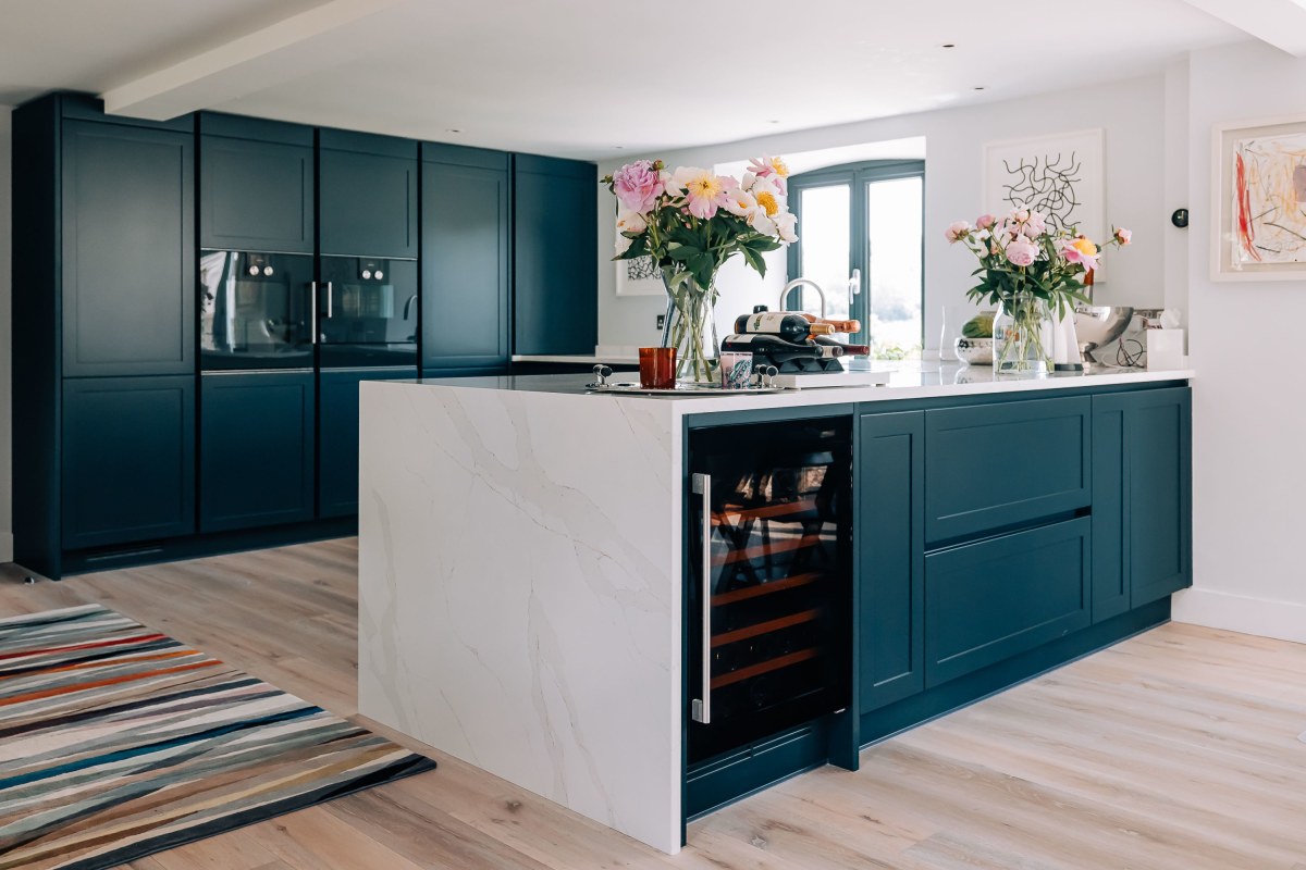 A kitchen island with white quartz waterfall worktop, and dark blue cabinetry