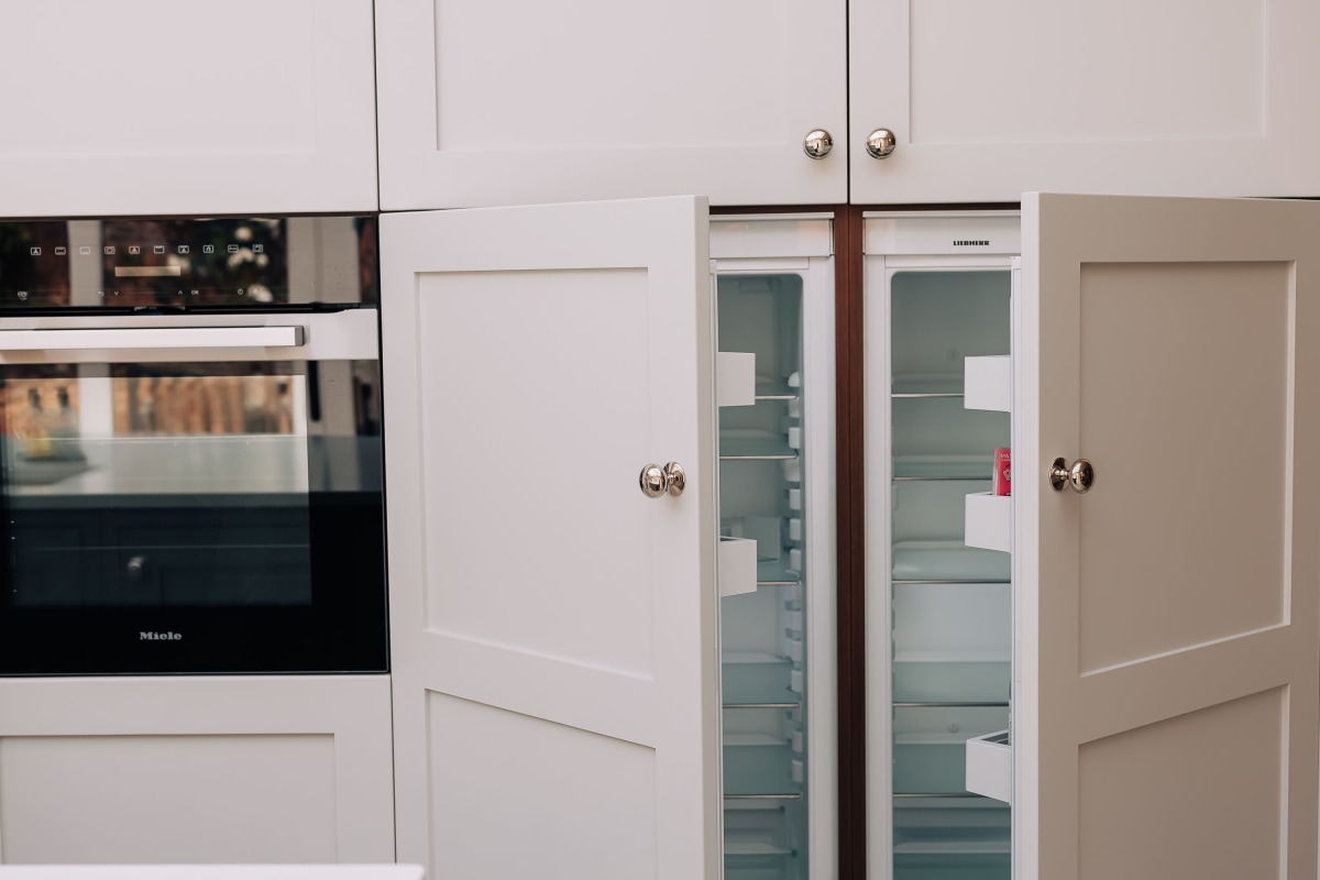 A bult in fridge freezer is open with cream shaker doors and an oven to the left side.