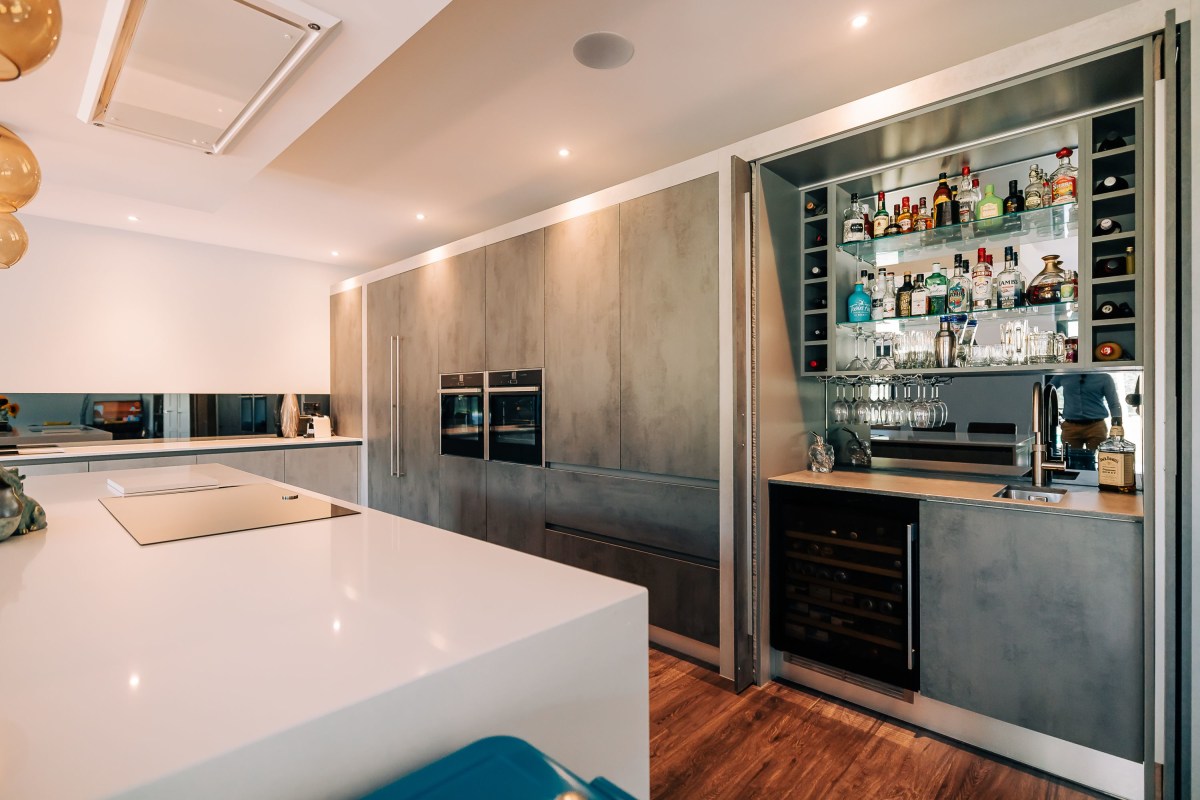 A pocket door bar space with mirrored back in an industrial style kitchen with white quartz worktops in Barnham