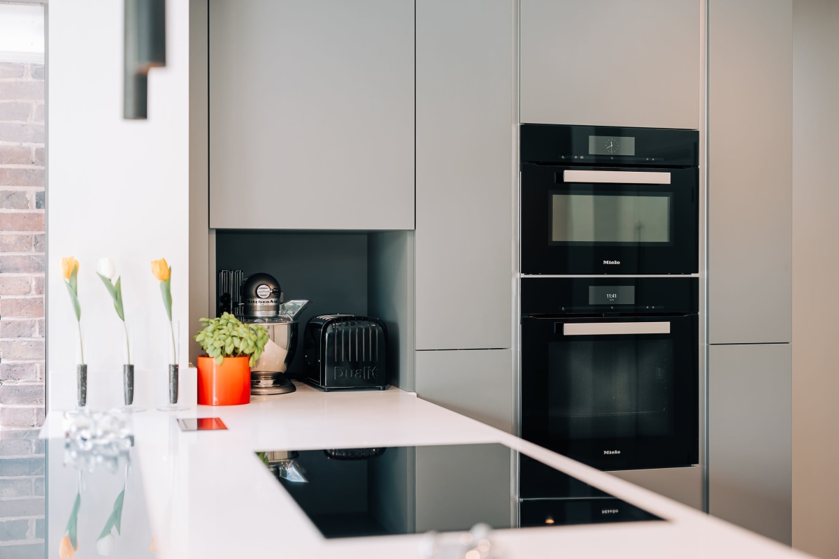 An induction hob on a white quartz peninsular with a bank of Miele ovens behind it