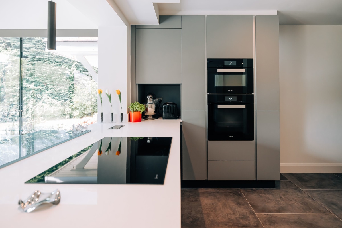 A kitchen island with blue mereway cabinetry, white quartz worktop with waterfall finish and white gloss tall units in the background