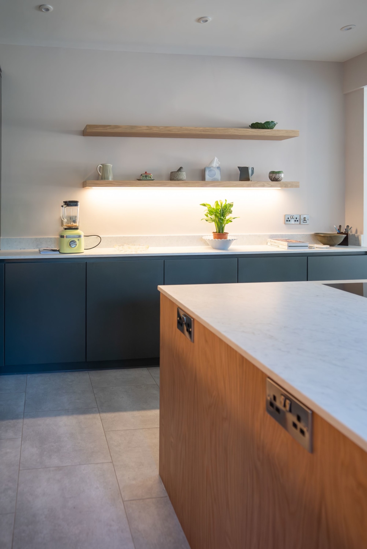 a kitchen island in wood with white quartz worktops and a dark green cabinet run in the background