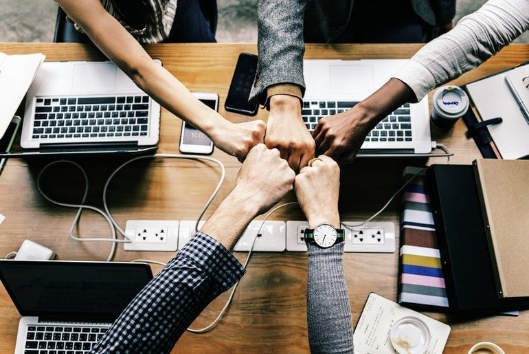 Quatre mains d'une équipe formant un fist bump au-dessus d'une table de travail avec des ordinateurs portables