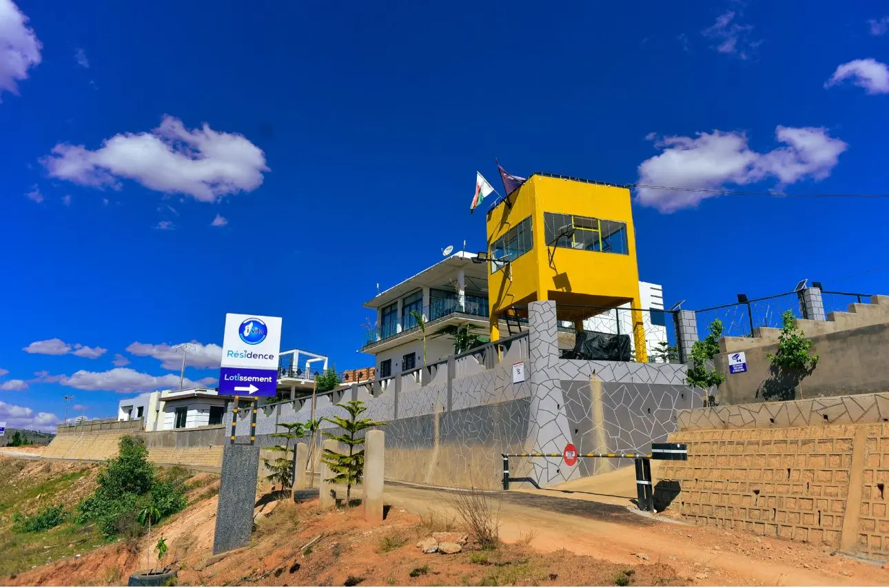 Vue extérieure de l'entrée sécurisée et de la guérite jaune du Domaine Résidentiel I-VITA à Madagascar