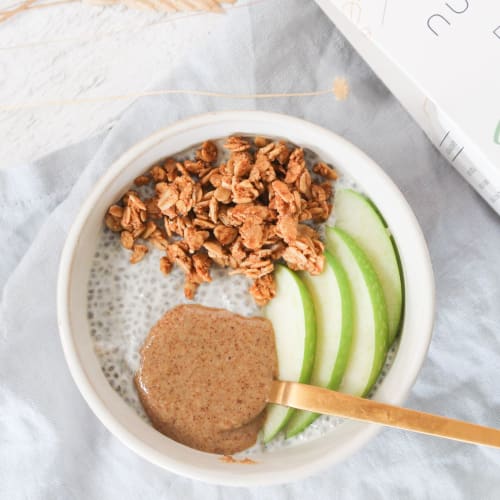 Bol pour le petit-déjeuner avec du pudding de chia, des morceaux de pomme, du granola bio et une cuillère de granola à tartiner