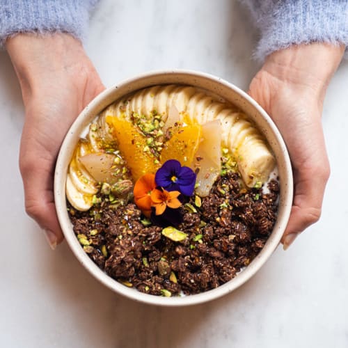 Bol pour le petit-déjeuner avec du pudding de chia, des morceaux de pomme, du granola bio et une cuillère de granola à tartiner