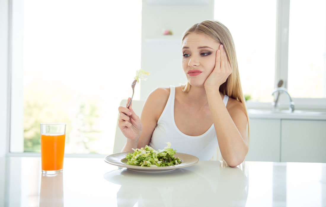 Woman eating greens looking unhappy