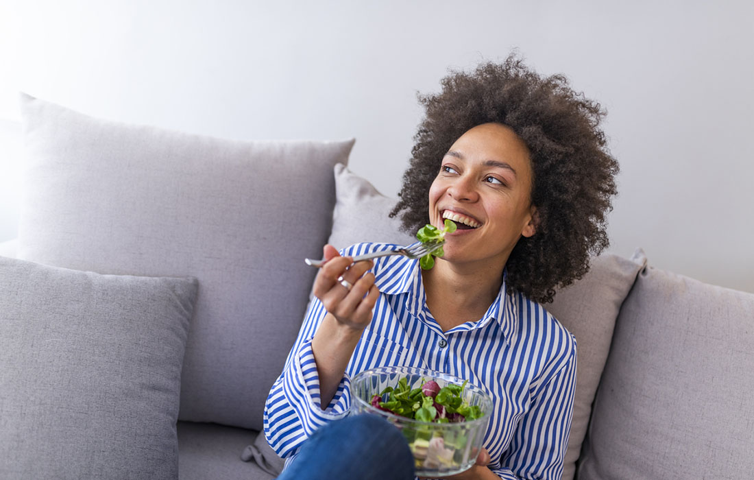 woman eating a bowl of salad on her couch