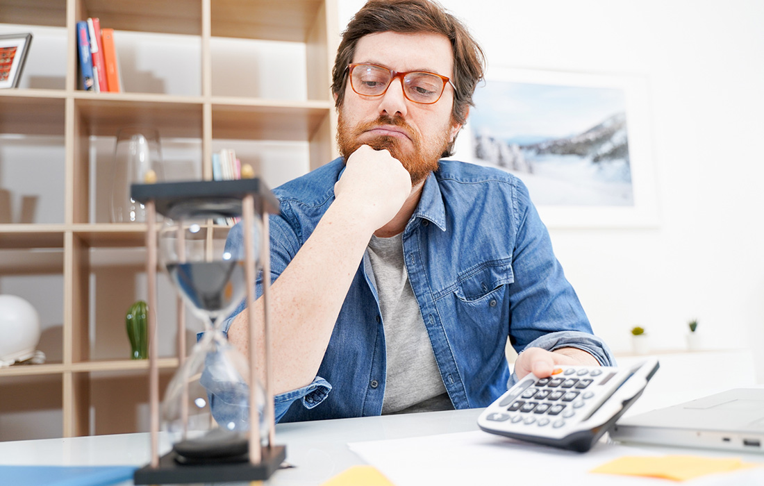 Man using calculator while looking at hourglass timer