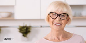 Older Female Patient Smiling with Dental Implants in Kitchen 300x150