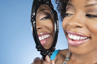 A woman examining herself for oral cancer by using a mirror.