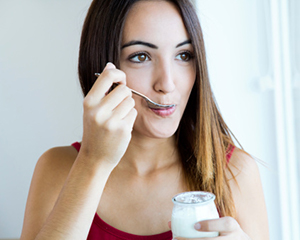 Image of a smiling woman eating yogurt after her oral surgery.