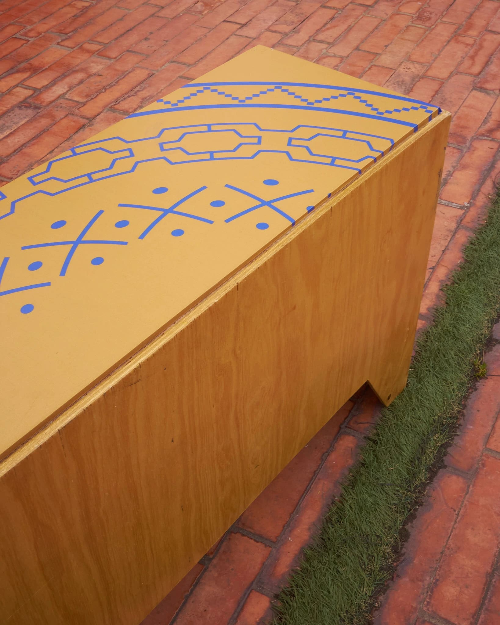 Banca de madera ocre con grecas e iconografía indígena