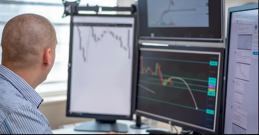 Multiple monitors displaying live CFD trading platform charts with candlestick patterns, price movements, and market data.