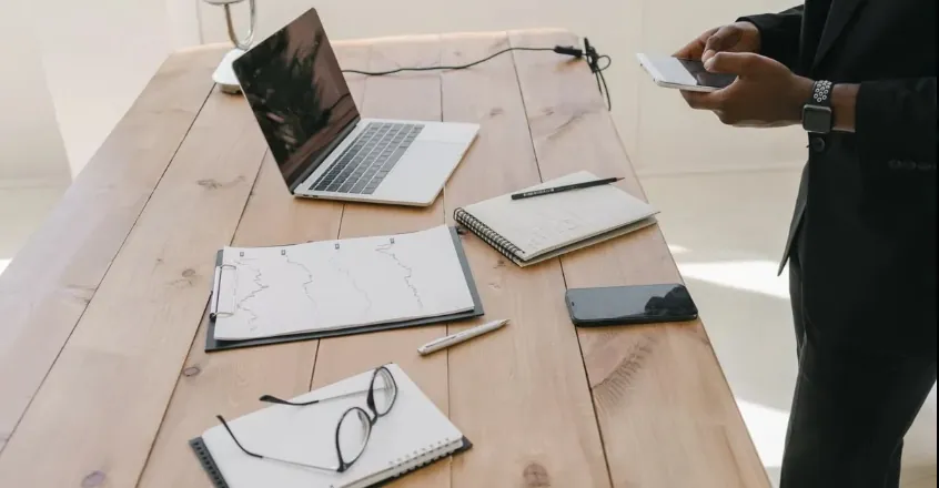 Professional trader reviewing CFD trading platform on laptop at organized wooden desk workspace.