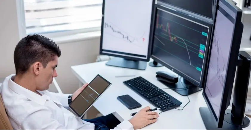 Trader analyzing multiple monitors displaying stock charts on copy trading platform at desktop setup.