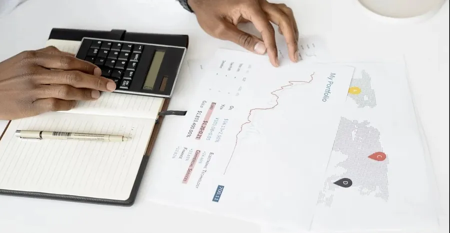 Person using calculator to analyze copy trading platform performance charts and financial data on desk.