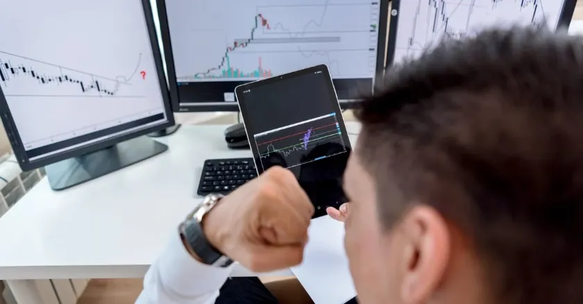 Trader analyzing forex charts on multiple screens including tablet and monitor displaying market data.