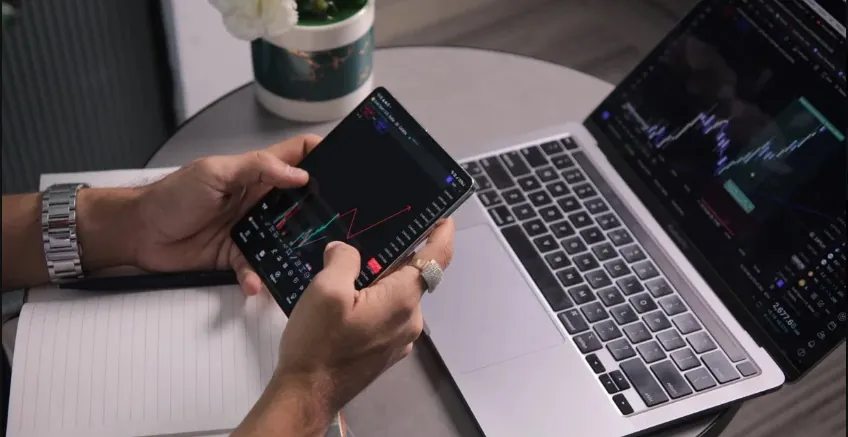 Trader checking best forex trading platforms on smartphone and laptop with live price charts at desk.