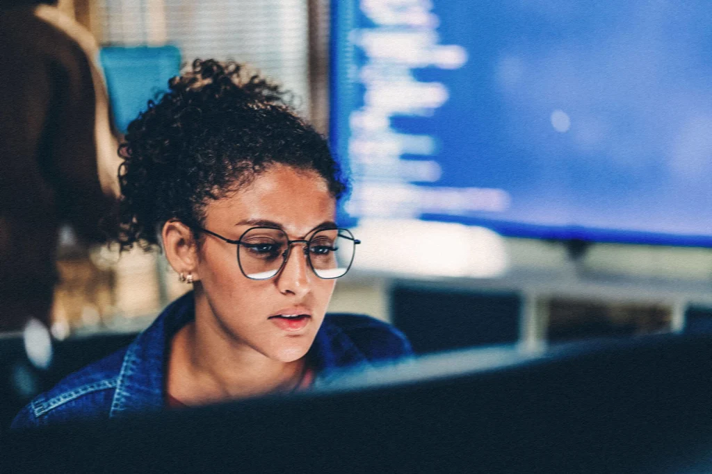woman with glasses looking at a desktop computer screen