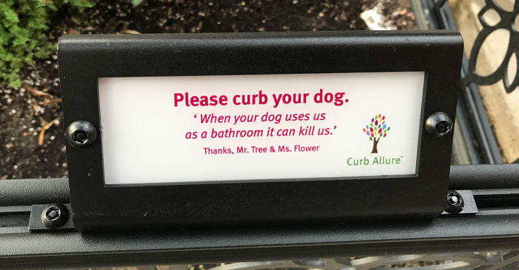 A sign that says “Please curb your dog. When dogs us as a bathroom it kills us.”