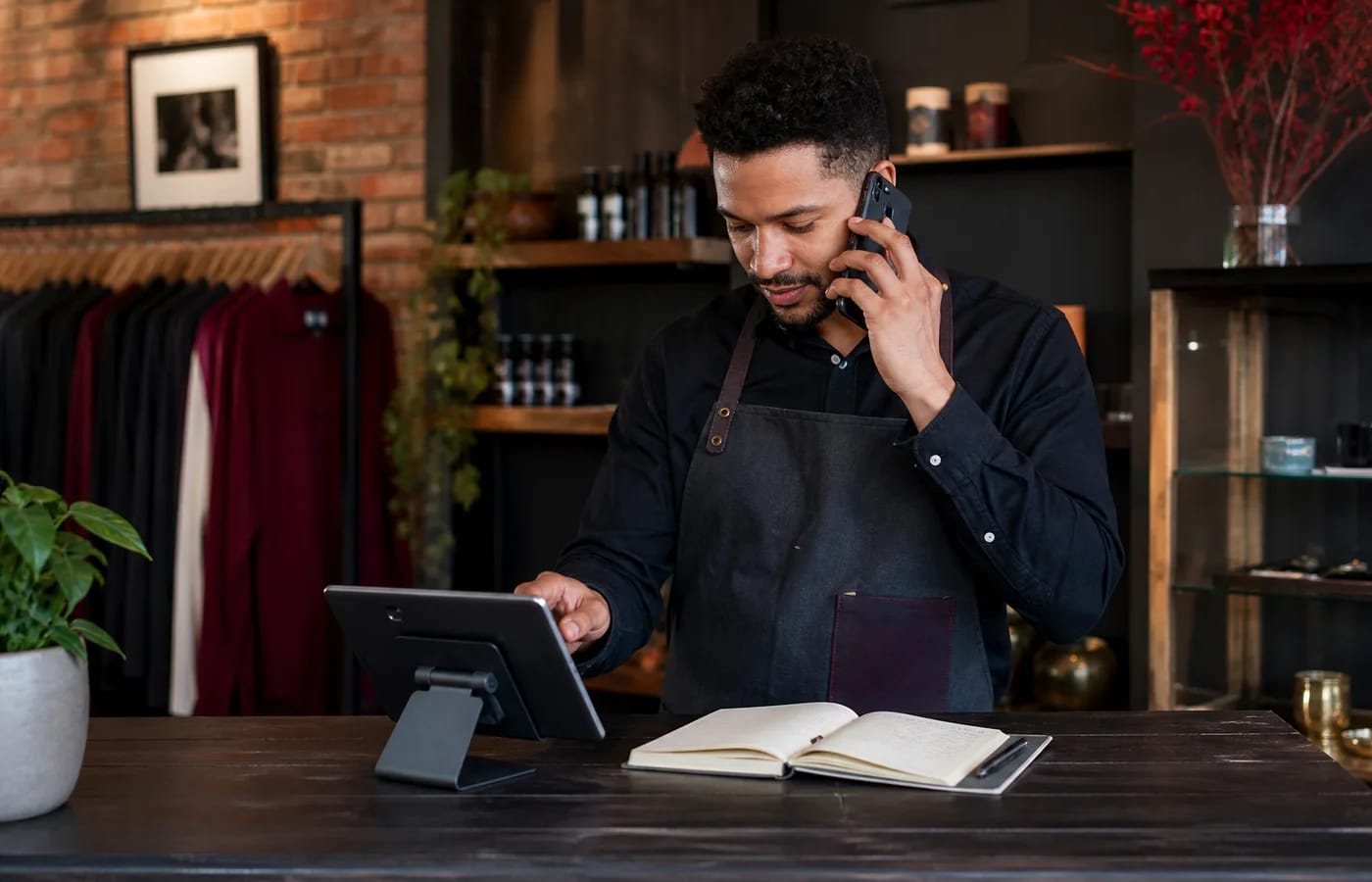 Local business owner managing customer enquiries at a shop counter with POS and phone