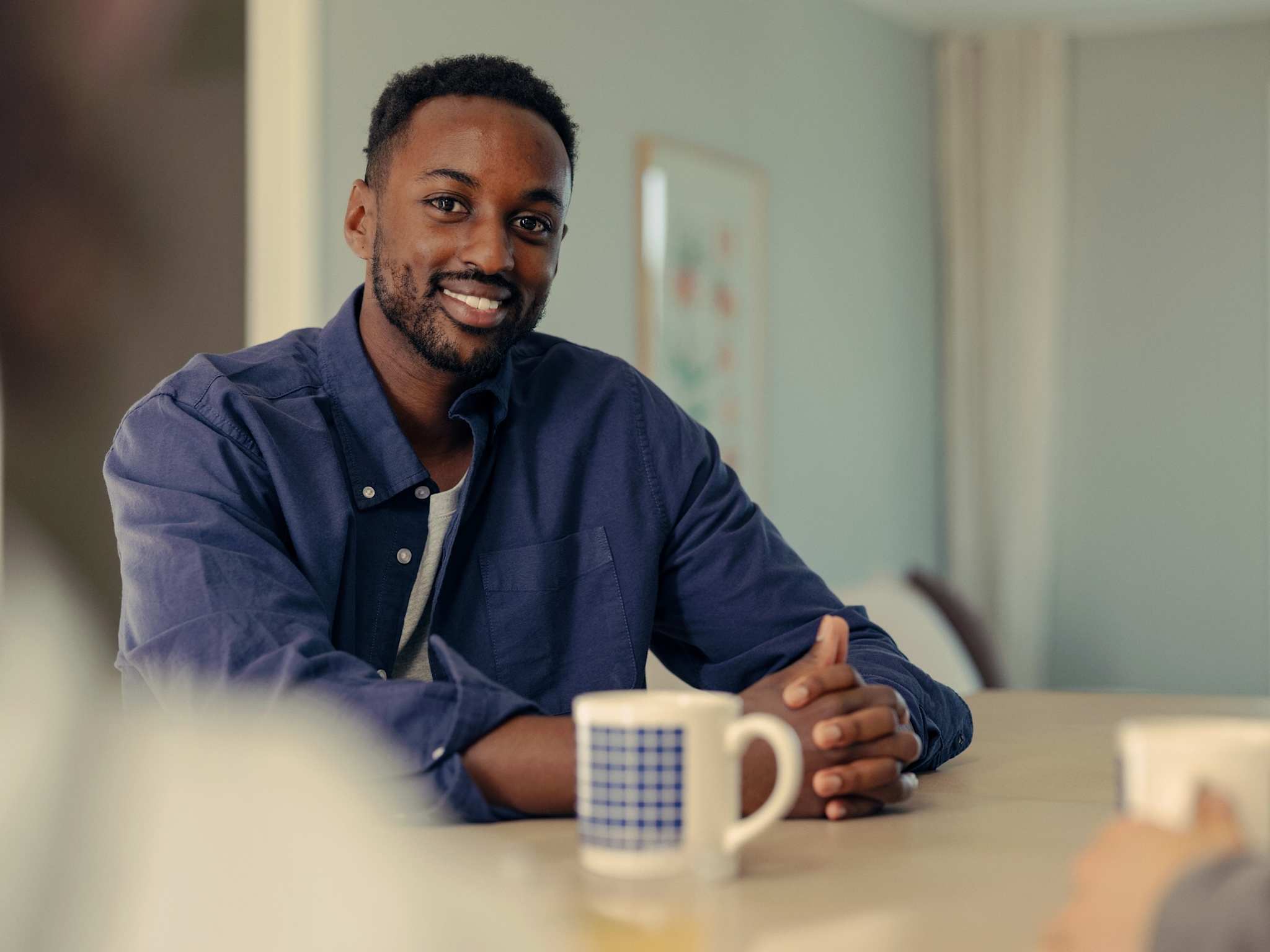 Mann sitter med en kaffekopp ved et bord og ser mot kamera