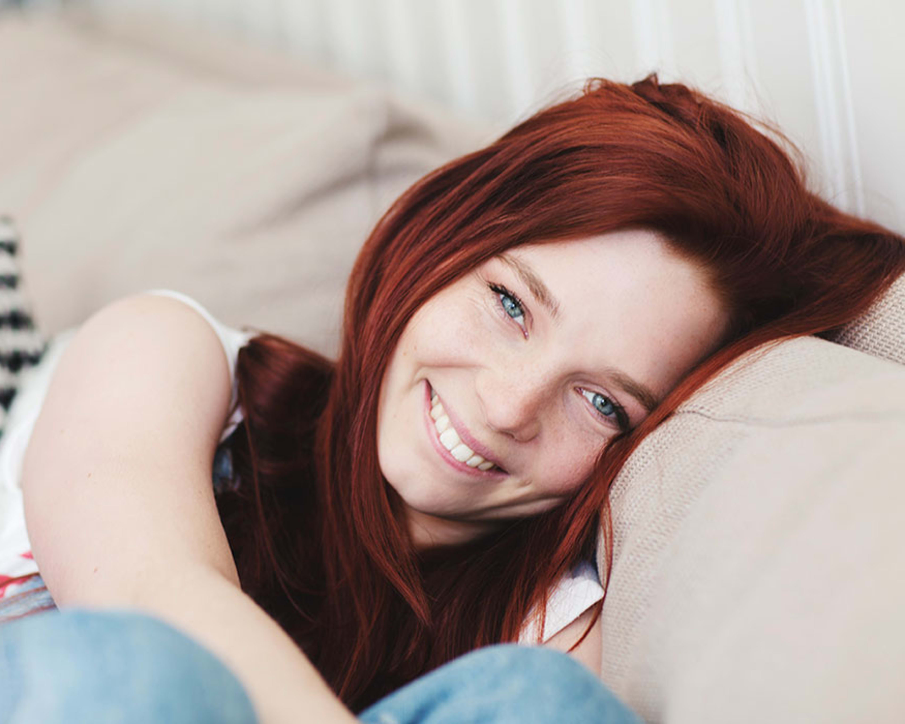 En smilende ung kvinne sitter i en beige sofa