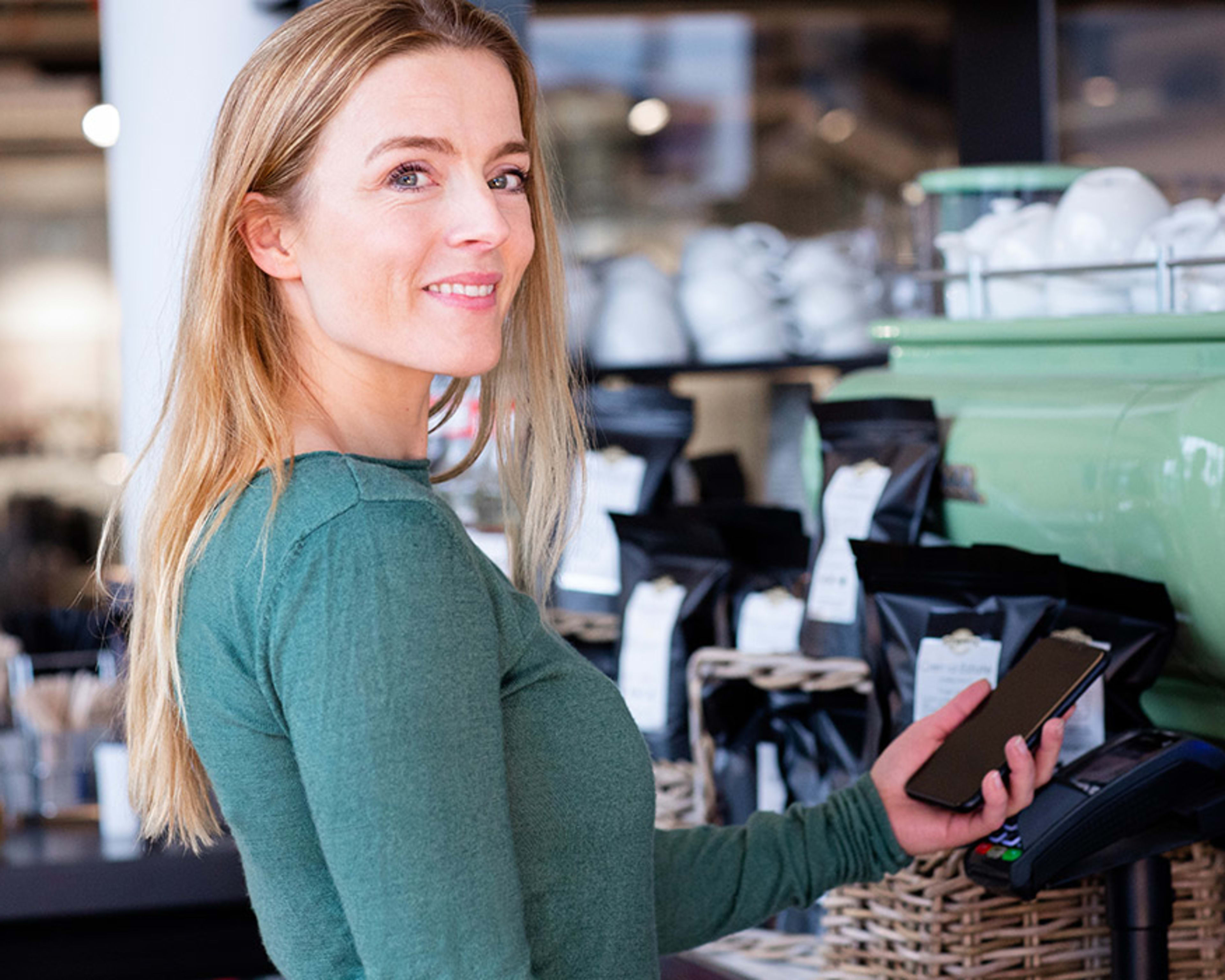 Dame i en kaffebar som betaler med bankkort på mobilen.