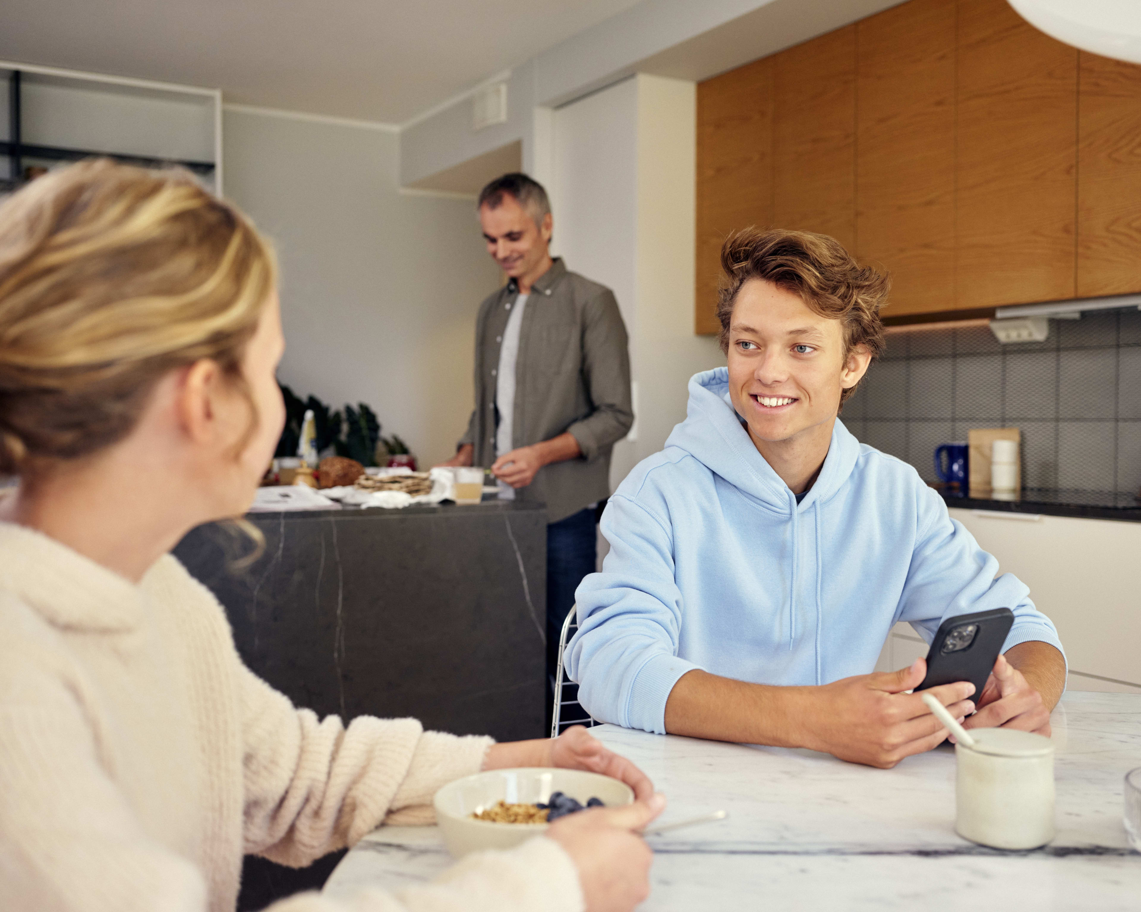 smilende gutt som sitter med telefonen i hånden og snakker med foreldrene sine