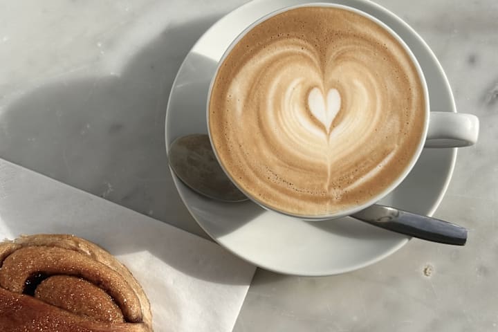 Bilde av en fersk kanelsnurr og en kopp kaffe.