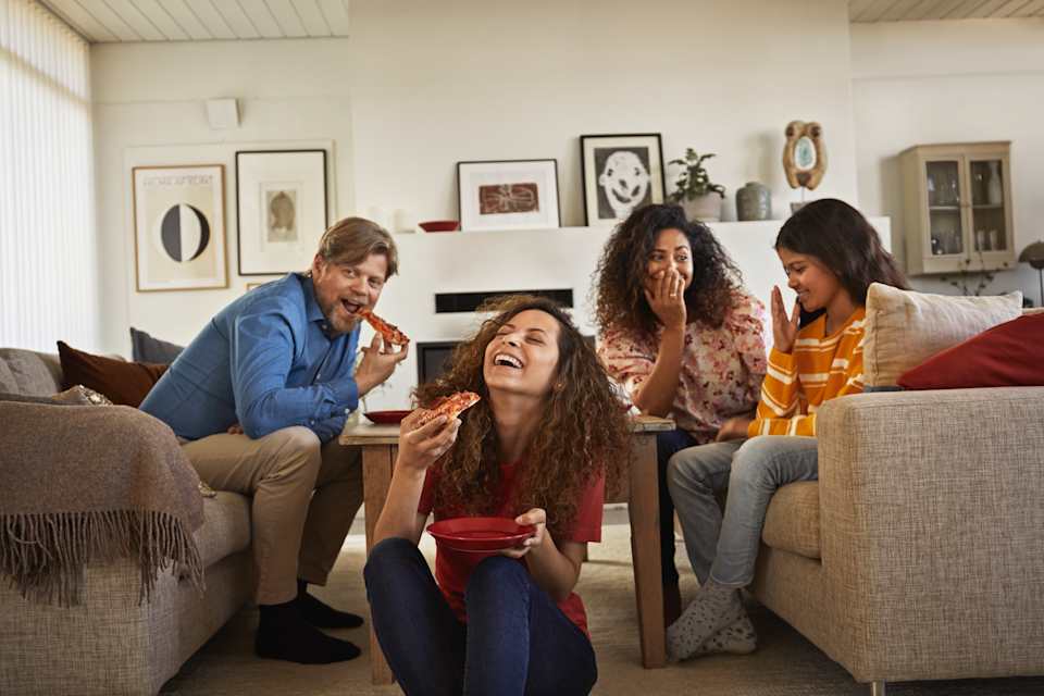 Fire personer ser på TV og spiser pizza.