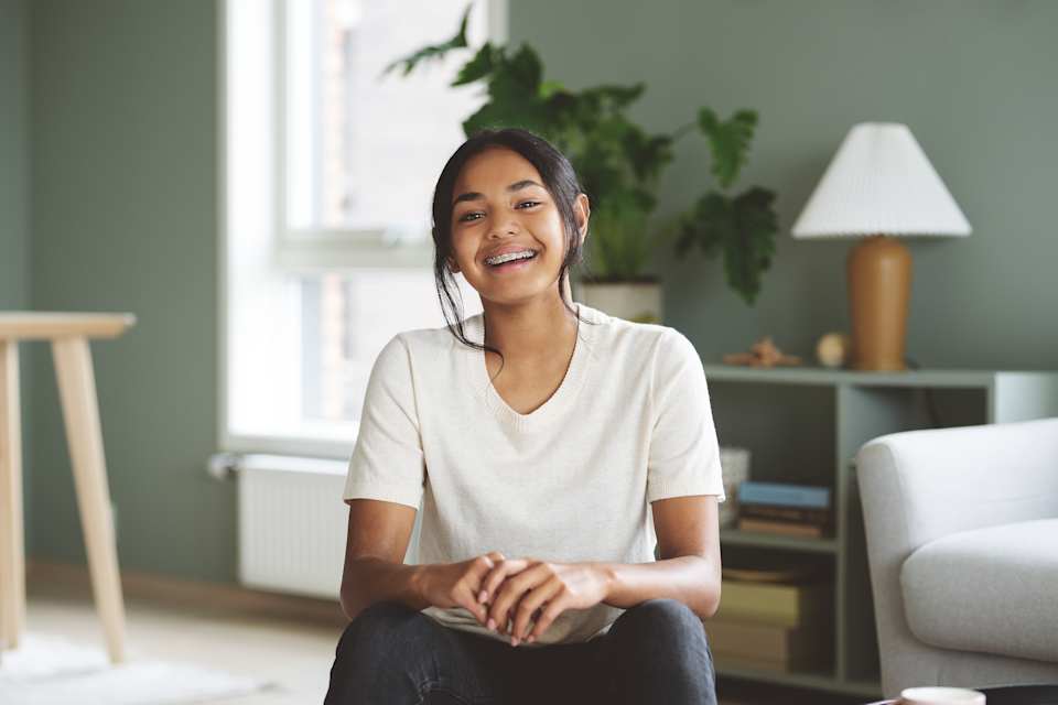 En ung jente sitte i en stue og smiler til kamera