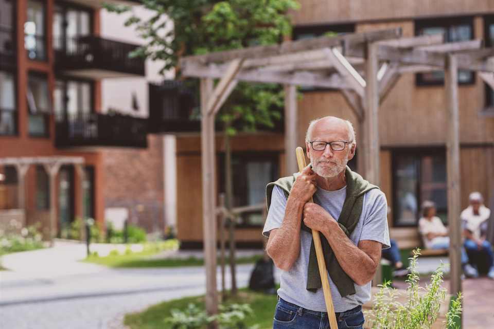 Mann som lener seg på en rake i bakgården