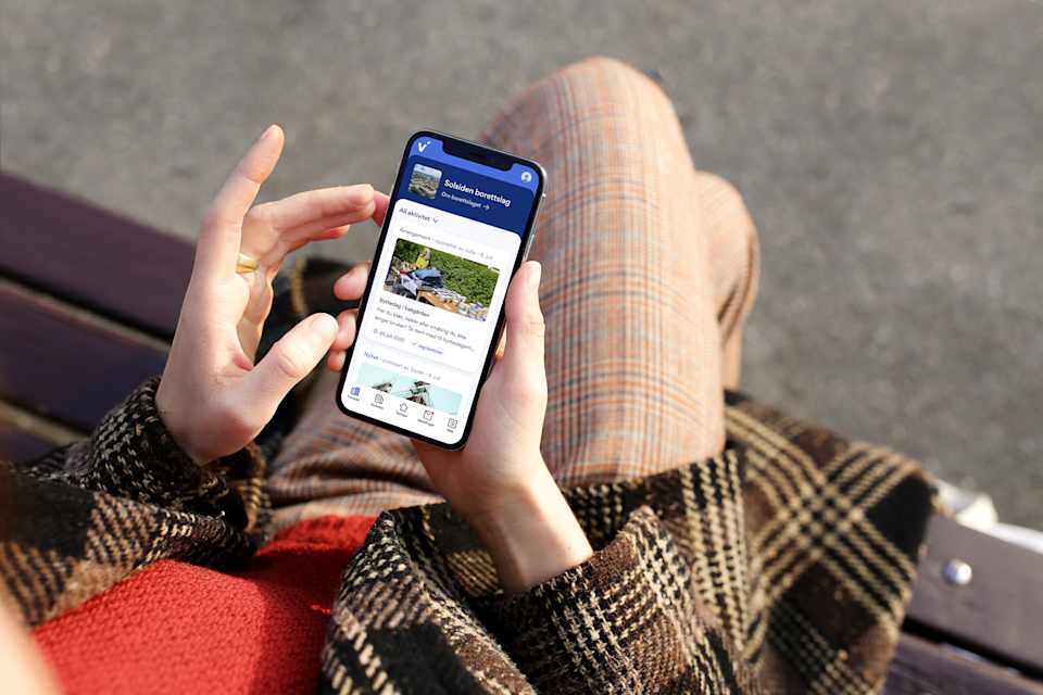 En dame sitter på en benk med en mobil i hånda og ser på Vibbo