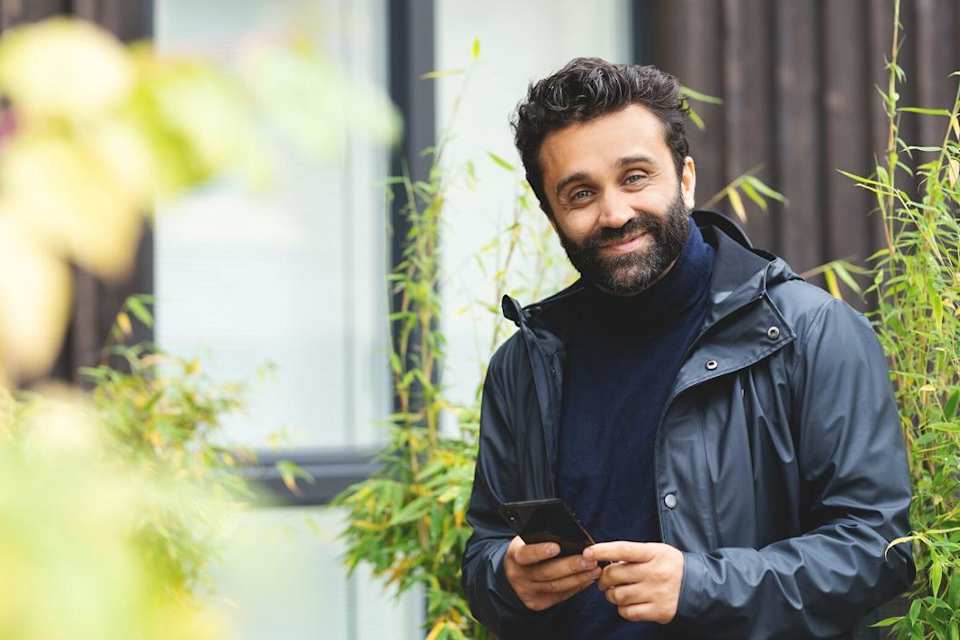 En mann står utenfor et hus og smiler mot kameraet.