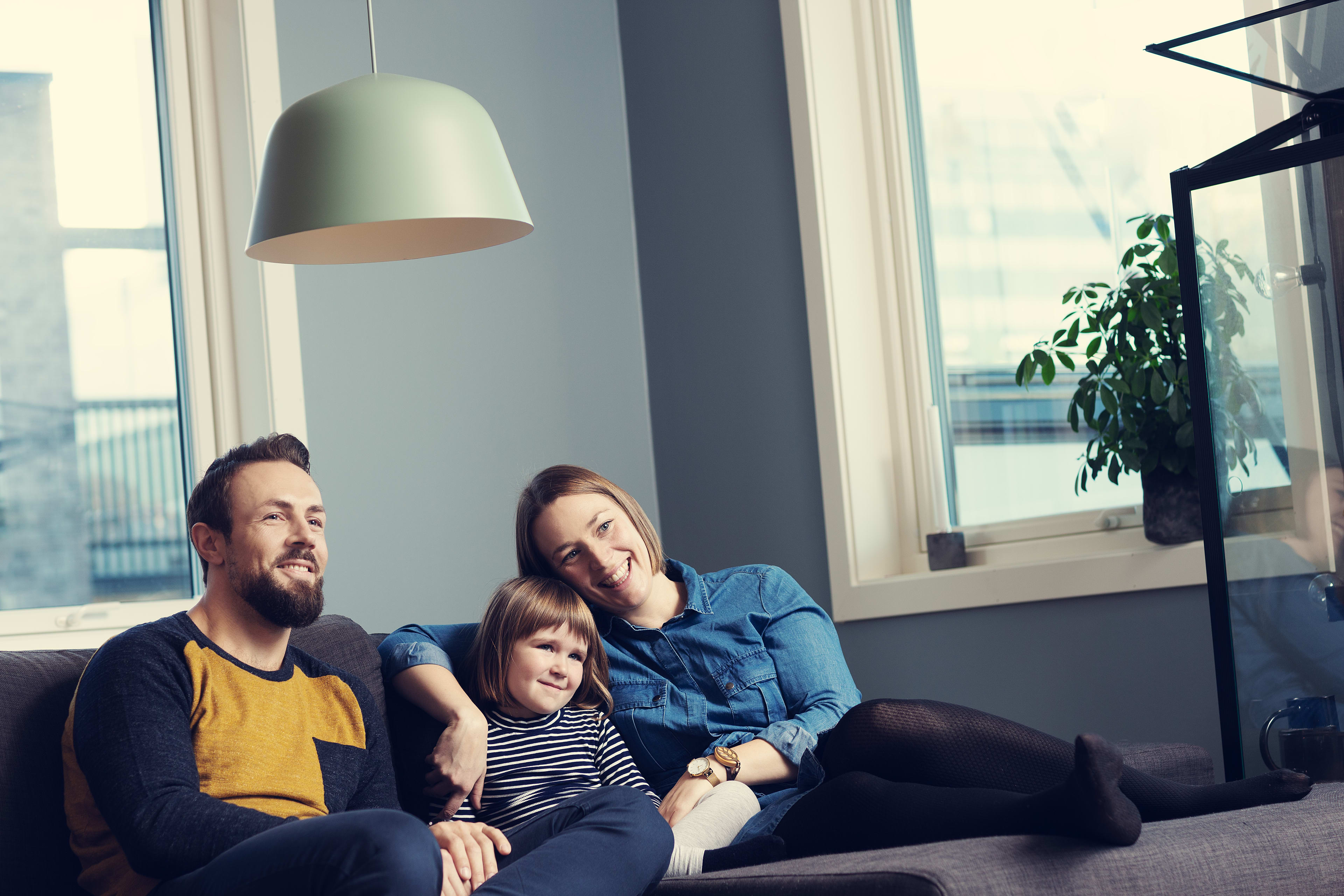 En familie på tre sitter i sofaen og ser på TV.
