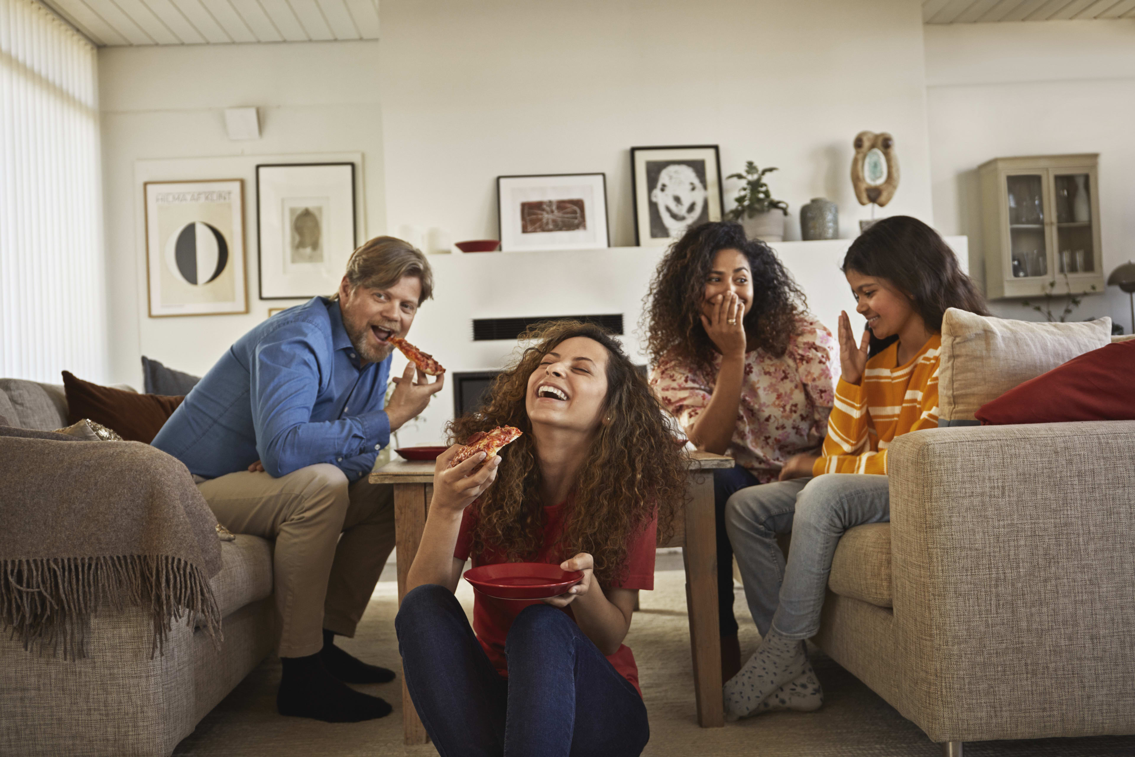 Fire personer ser på TV og spiser pizza.