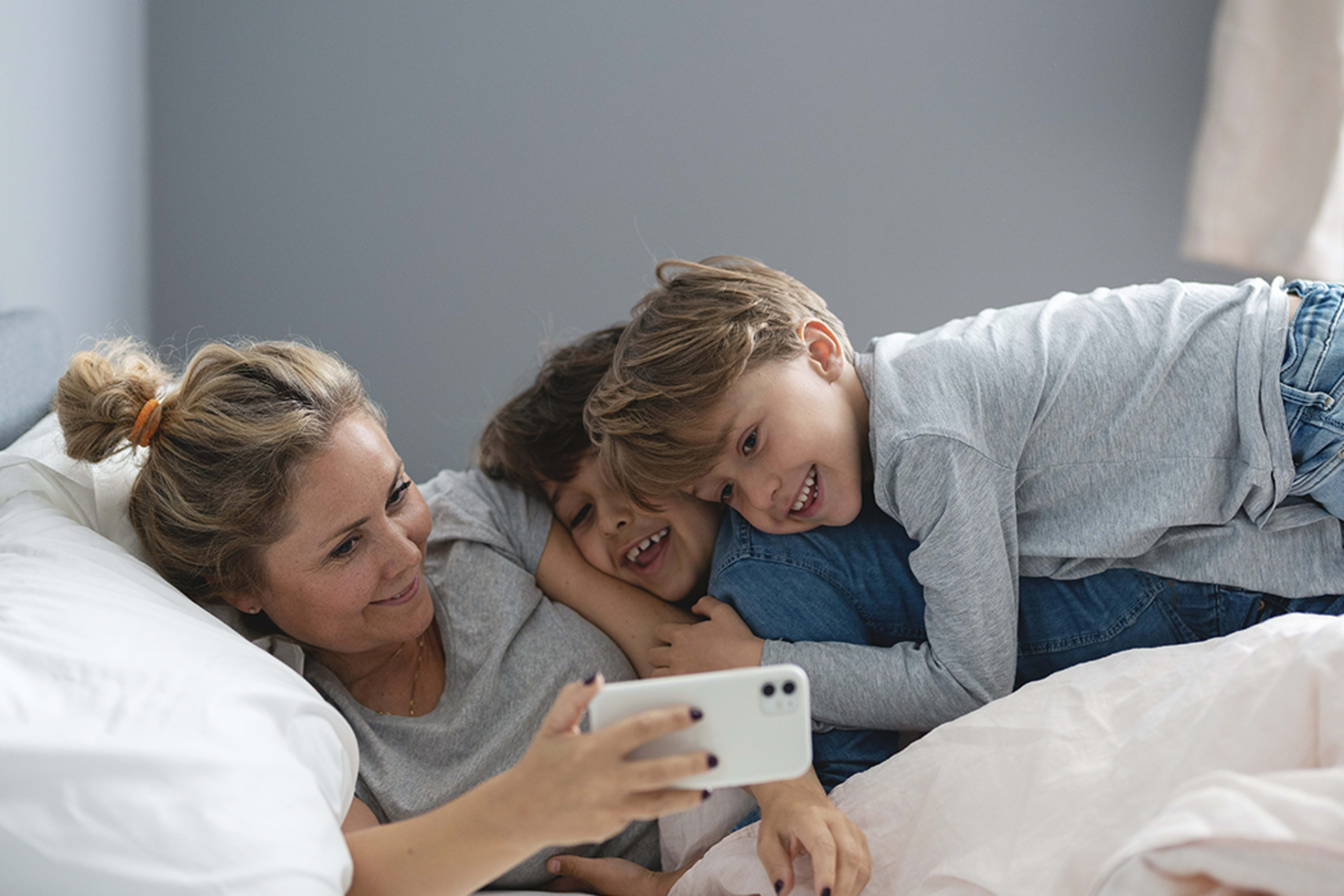 Mor og barn ligger i senga og ser på noe på mobilen til moren sammen.