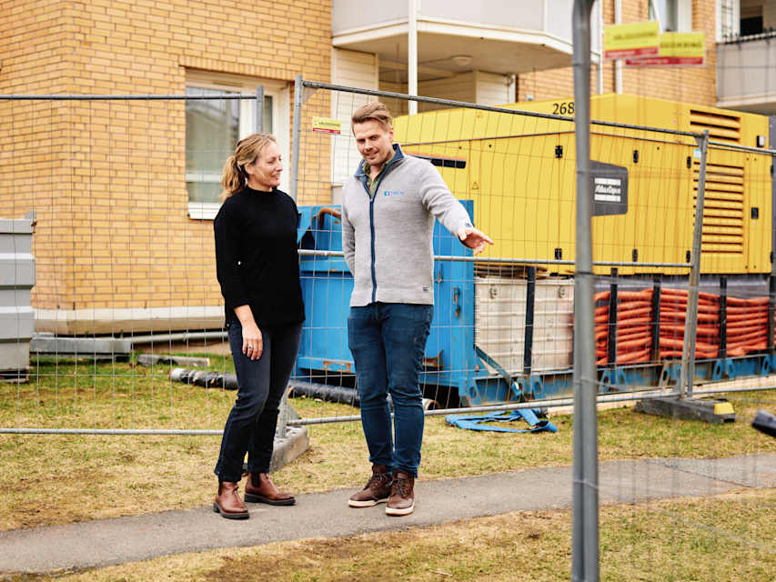 To personer står utenfor en boligblokk som er under rehabilitering