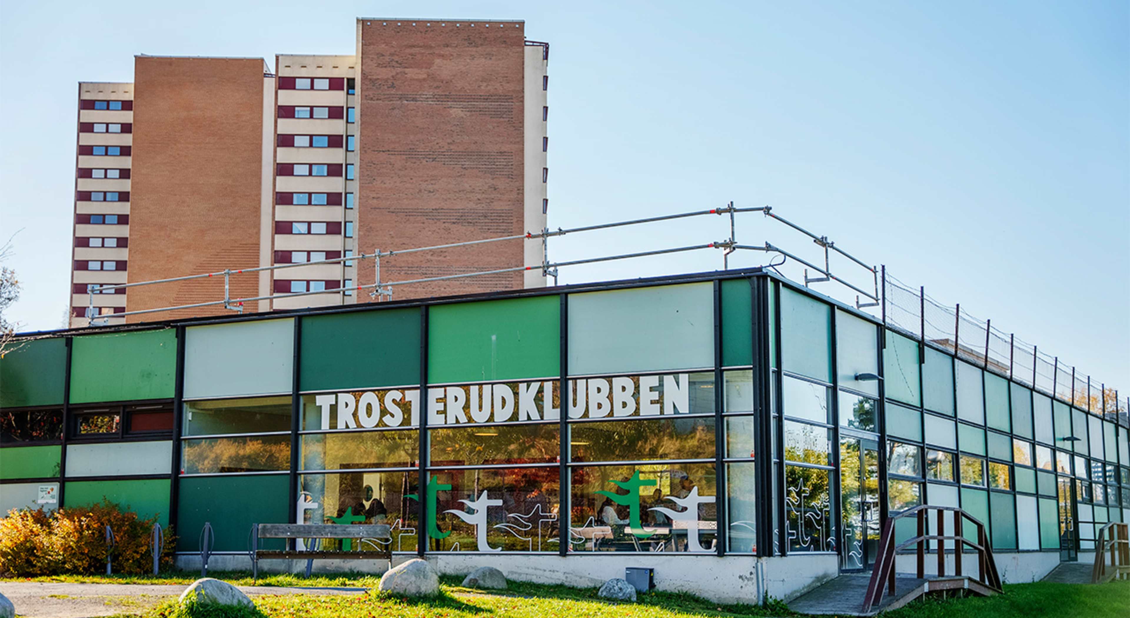 Fasadefoto av bygget til Trosterudklubben. I bakgrunnen ser vi en en av boligblokkene på Trosterud.