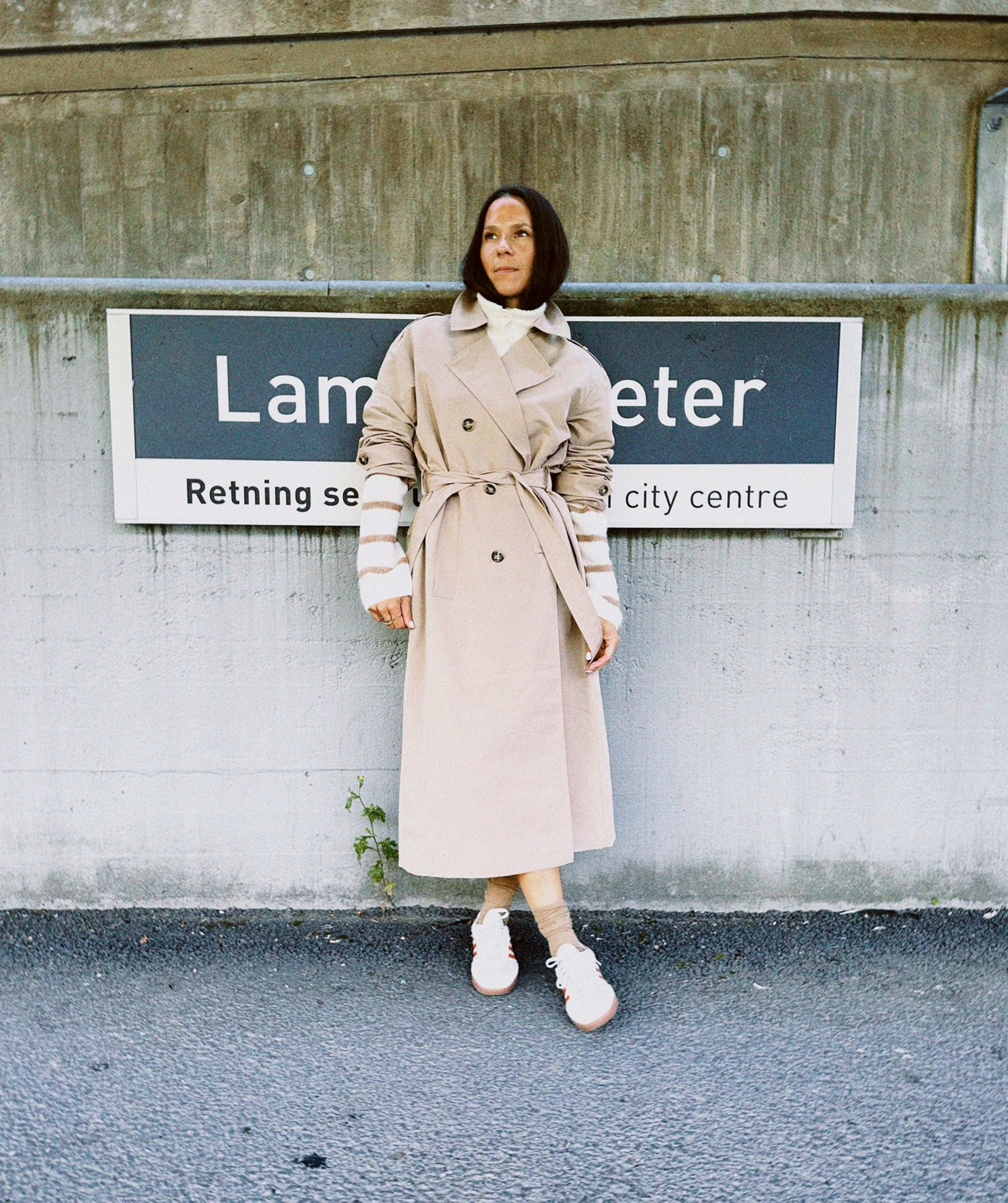 dame i lys lang trenchcoat, hvit genser og sneakers