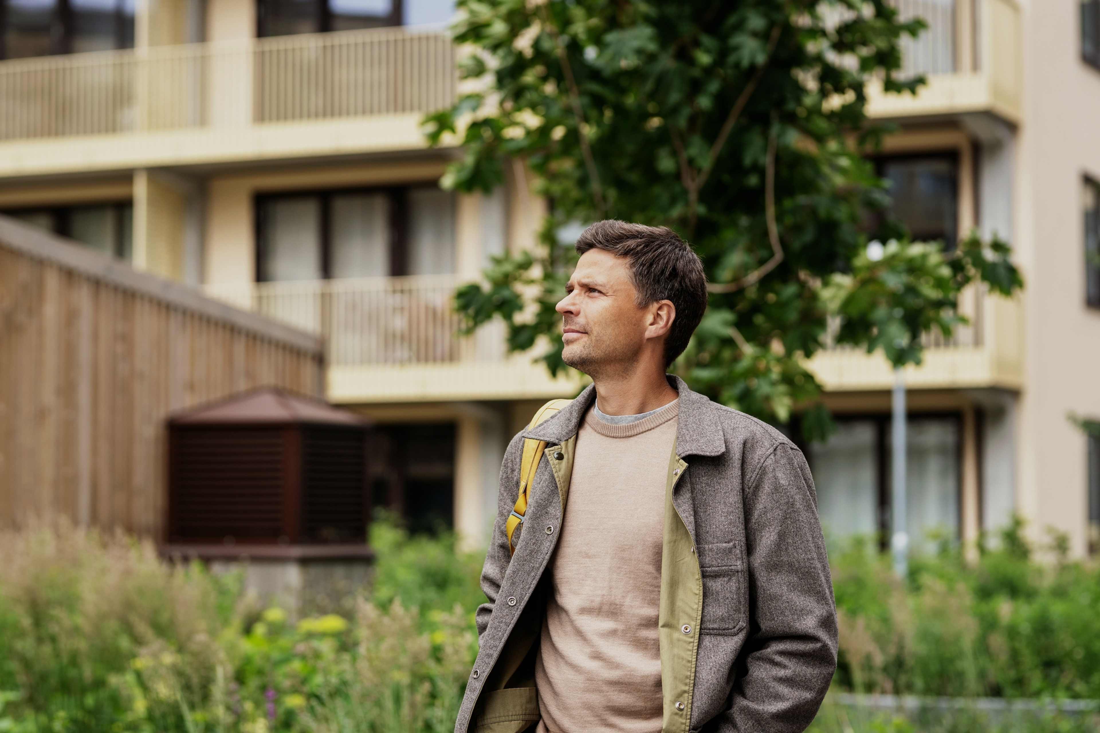 Mann står utenfor en boligblokk og ser opp mot fasaden.