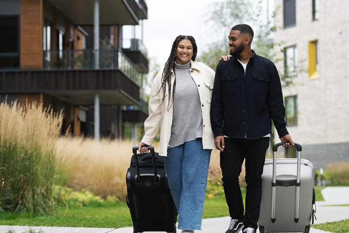 En mann og en kvinne triller koffertene sine utenfor der de bor. De smiler og er glade. de skal ut å reise.